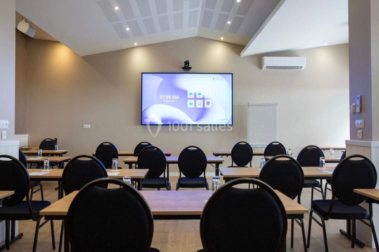 Salle de réunion équipée de tables, chaises, écran de projection allumé, climatisation et éclairage au plafond.