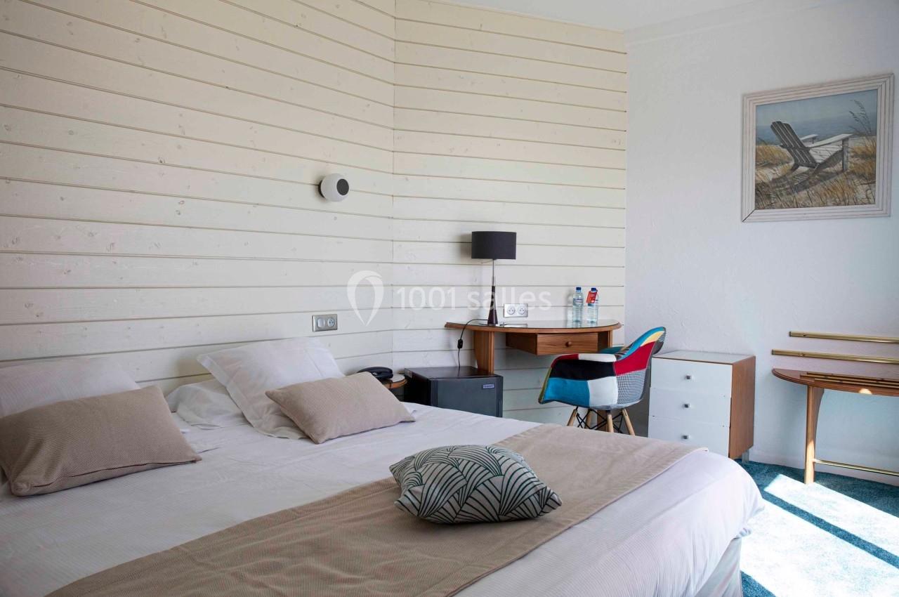 Chambre lumineuse avec lit double, bureau en bois, chaise colorée et décoration murale sur un mur en lambris blanc.