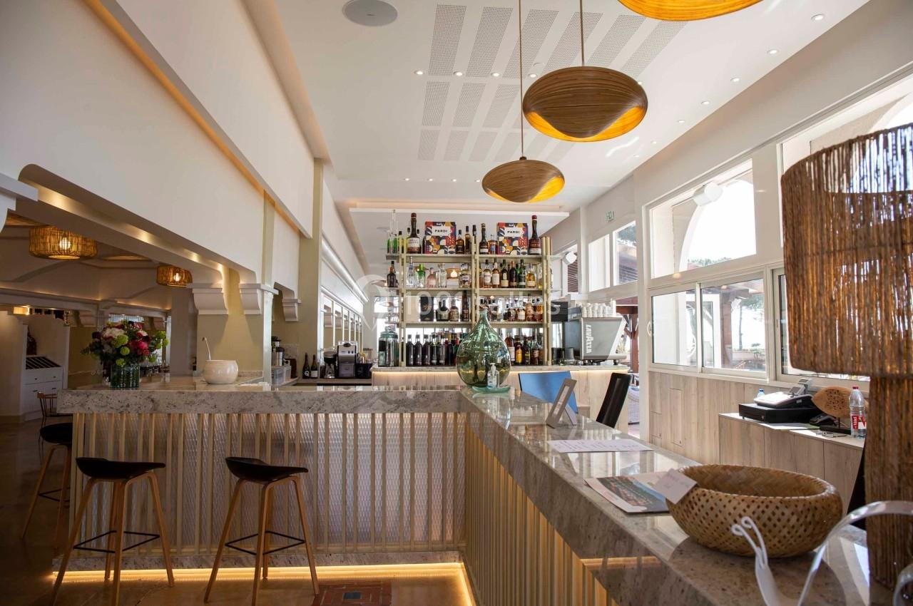 Intérieur d'un bar lumineux avec comptoir en marbre, étagères de bouteilles, tabourets et décorations en bois.