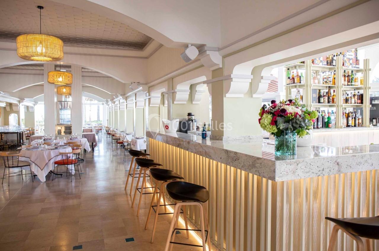 Salle de restaurant lumineuse avec un bar en marbre, des tabourets en bois et des tables dressées en arrière-plan.