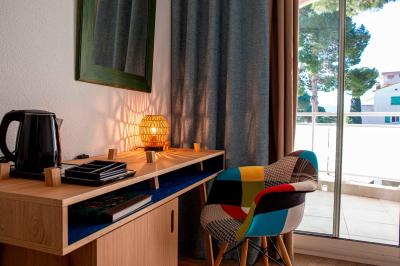 Miniature Location salle Saint-Cyprien (Pyrénées-Orientales) - Grand Hôtel du Lido #9 Bureau en bois avec lampe allumée, chaise colorée et vue sur un balcon donnant sur des arbres et des bâtiments.