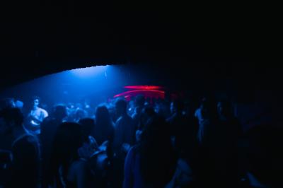 Salle sombre avec murs en briques, éclairage tamisé, scène en bois et tables basses au premier plan.