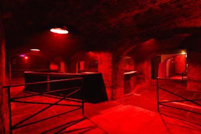 Salle sombre avec murs en briques, éclairage tamisé, scène en bois et tables basses au premier plan.