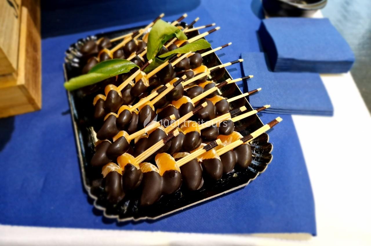 Plateau de brochettes de fruits enrobés de chocolat, présenté sur une nappe bleue avec des serviettes assorties.