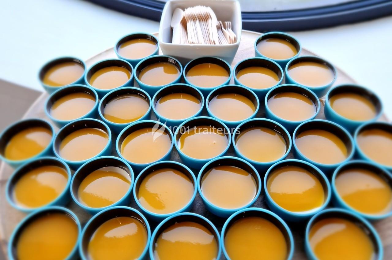 Petits bols bleus remplis de crème caramel disposés sur un plateau rond, avec des piques en bois dans un récipient.