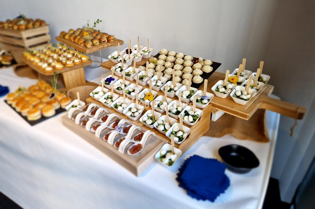 Buffet de petites bouchées salées et sucrées présentées sur des plateaux en bois, disposés sur une nappe blanche.