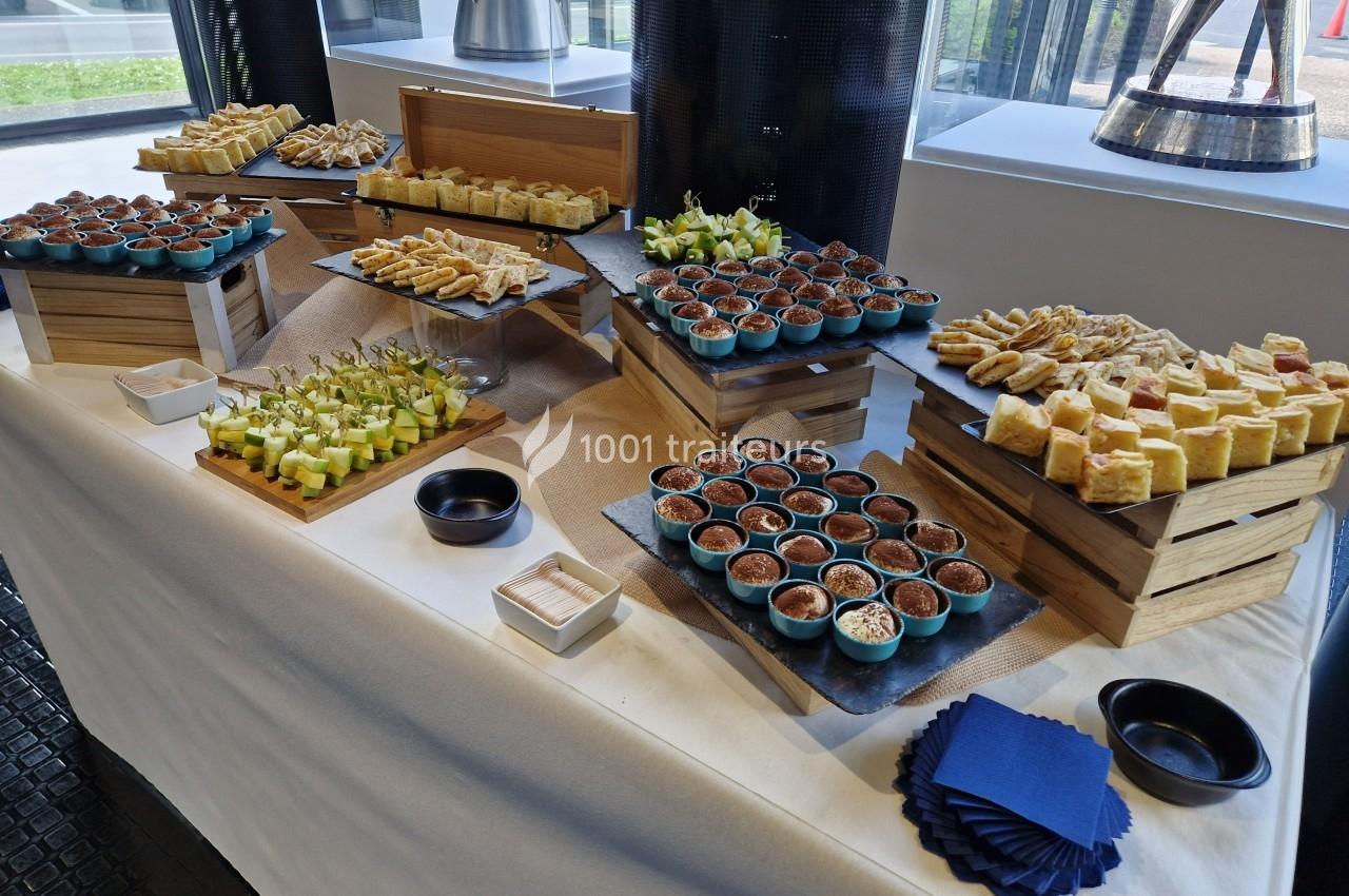 Buffet composé de verrines, amuse-bouches et petits fours disposés sur des présentoirs en bois dans une salle lumineuse.