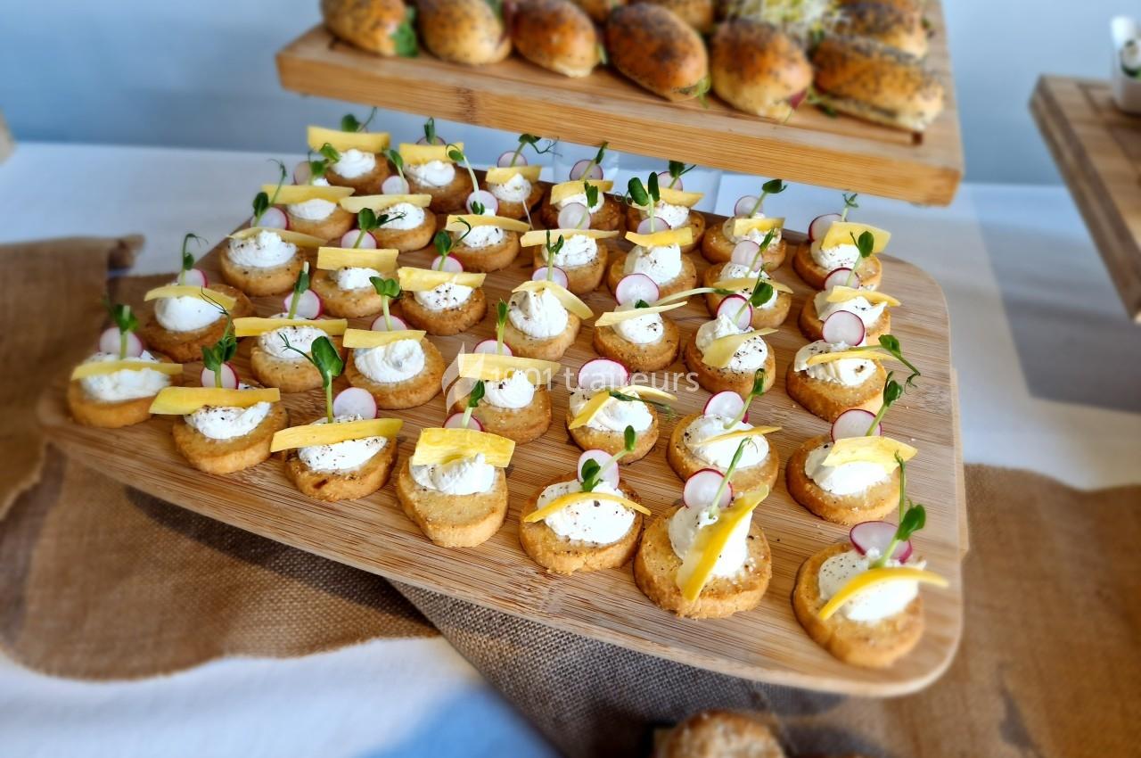 Plateau de bouchées apéritives garnies de fromage frais, radis, herbes et tranches de fromage sur une table.
