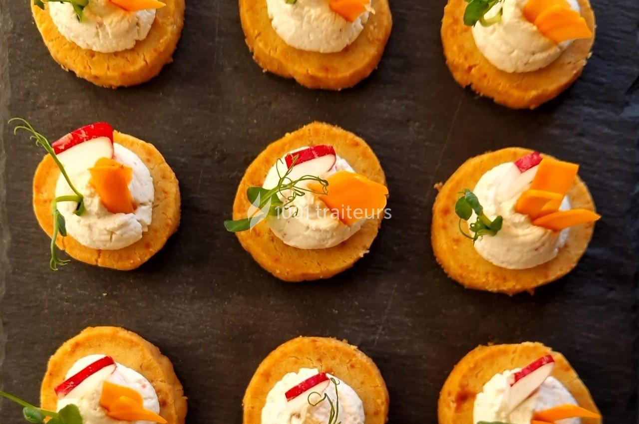 Bouchées apéritives disposées sur une ardoise, garnies de fromage frais, légumes et herbes fraîches.