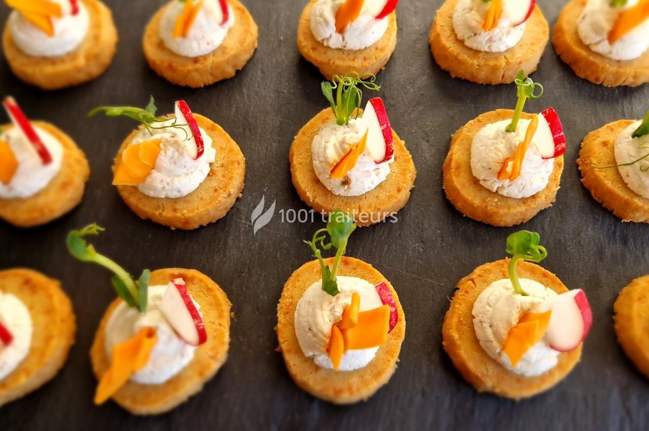 Assortiment de canapés sur une ardoise, garnis de crème et décorés de légumes colorés.