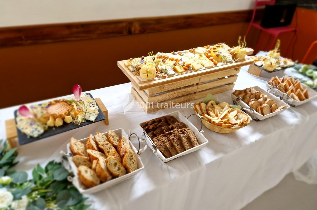 Table dressée avec un buffet de fromages variés, pains et accompagnements, disposés sur des plateaux et nappes blanches.