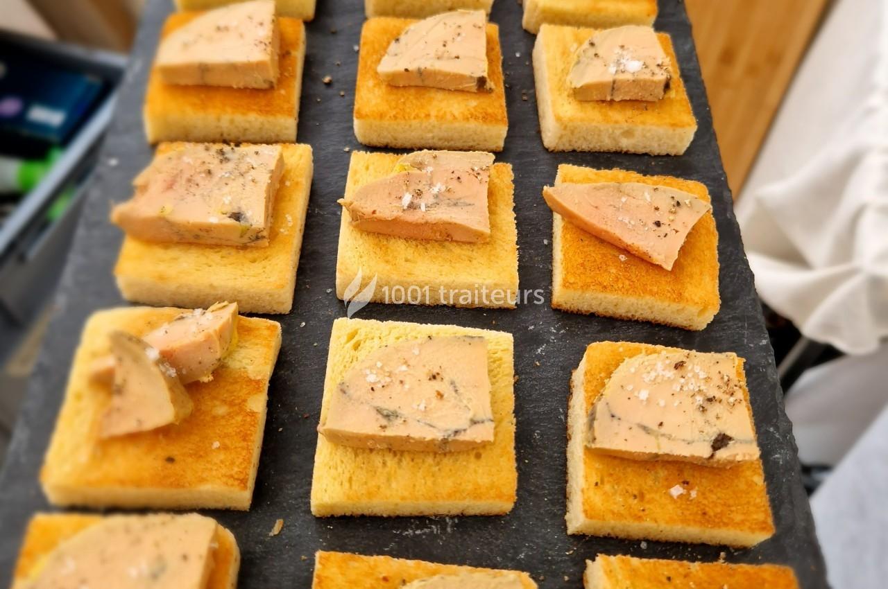 Tranches de foie gras posées sur des toasts dorés, disposés sur une ardoise noire.