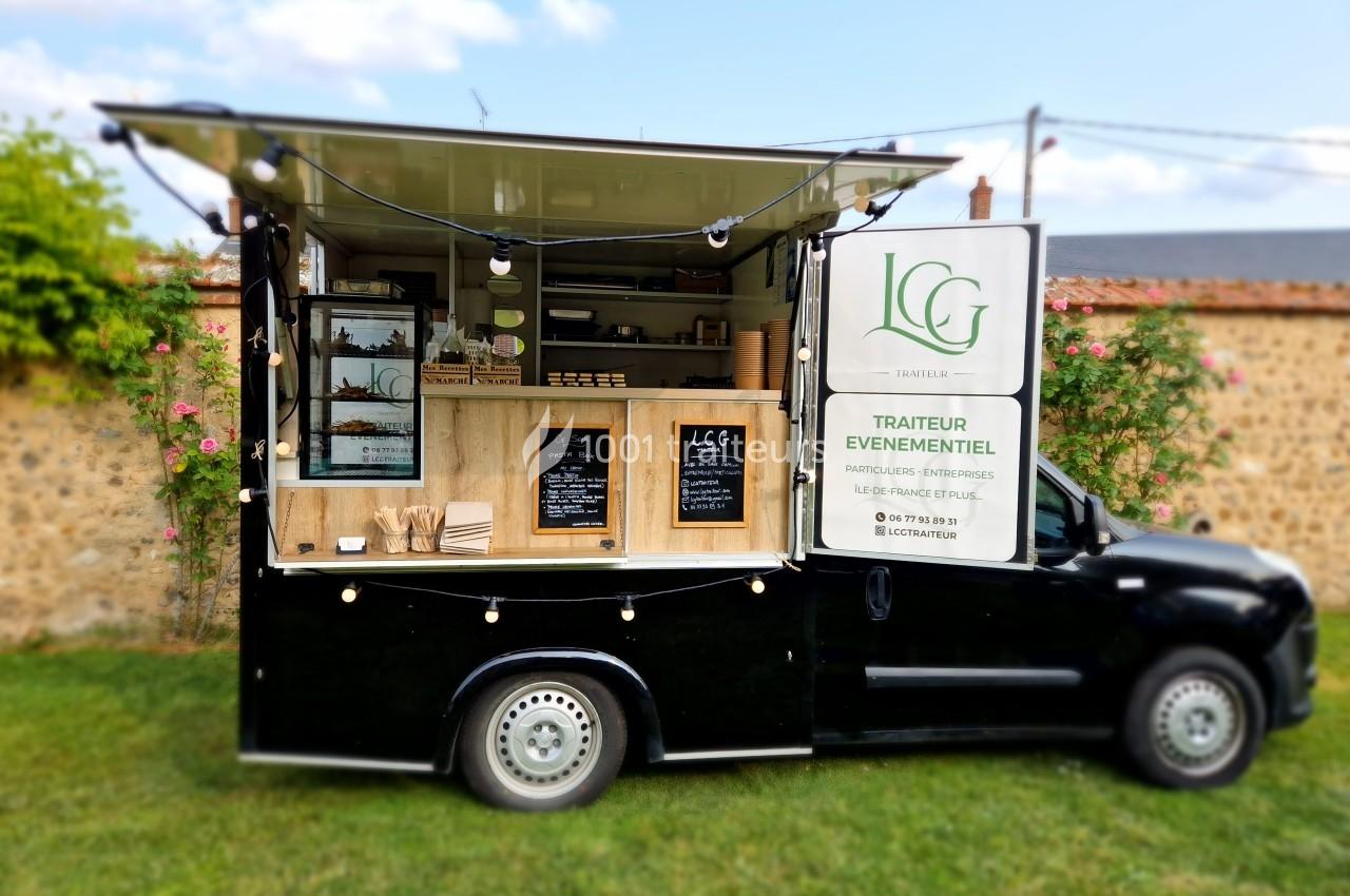 Camion noir aménagé en food truck, avec guirlandes lumineuses et étagères exposant des produits, stationné sur une pelouse.