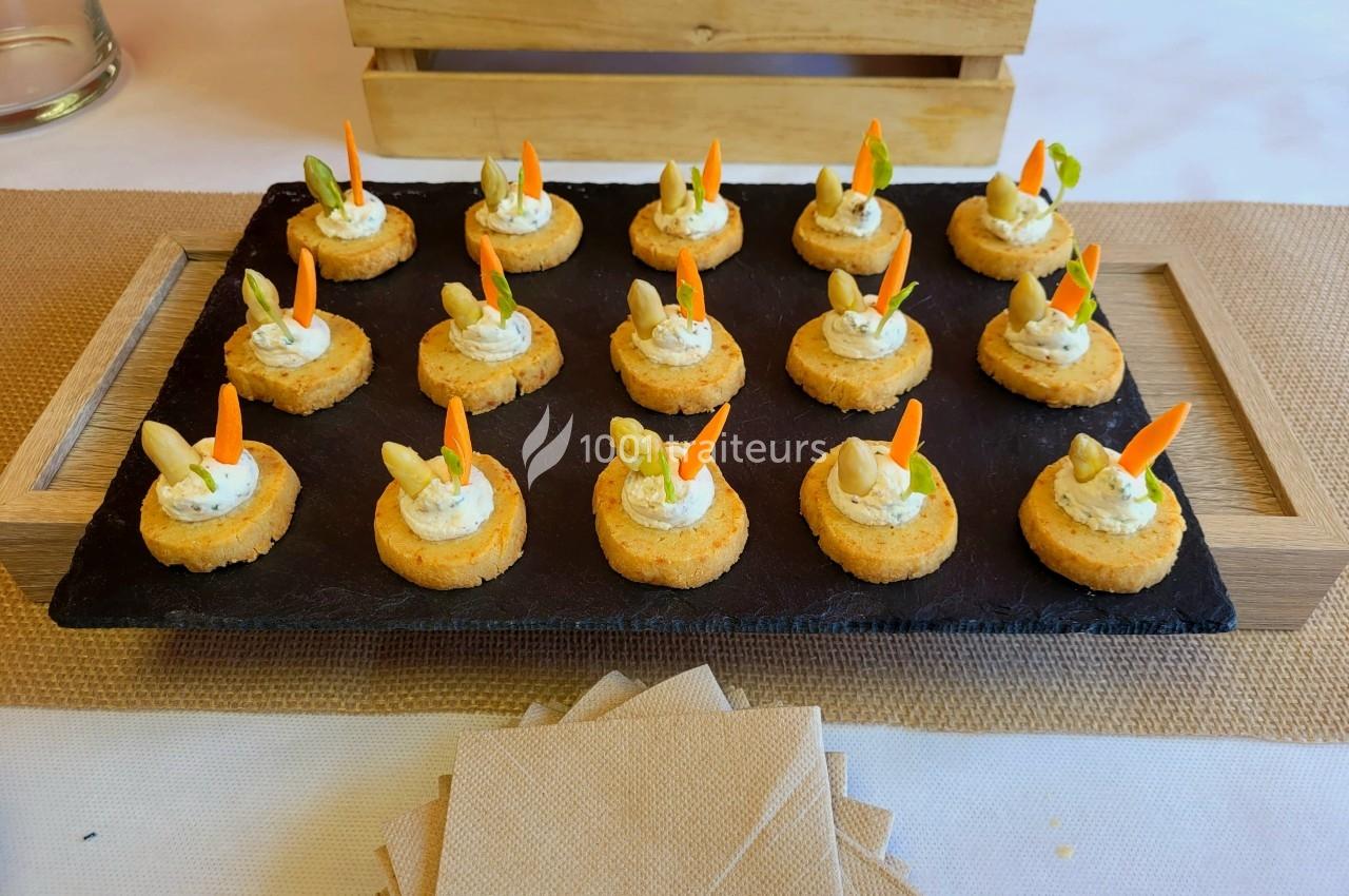 Plateau d'amuse-bouches sur ardoise, garnis de crème et décorés de légumes, présenté sur une table avec serviettes.