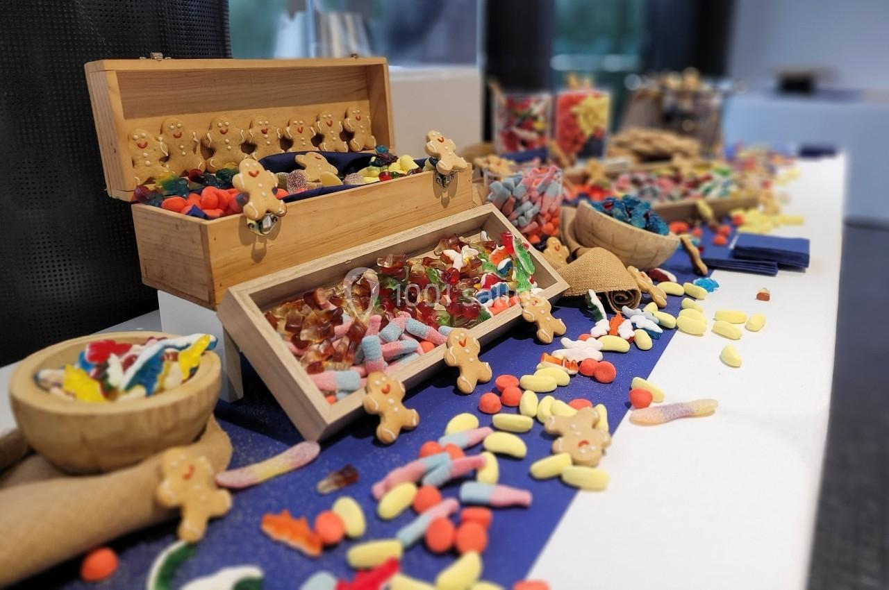 Buffet coloré de bonbons variés, avec des boîtes en bois ouvertes et des friandises répandues sur une nappe bleue.