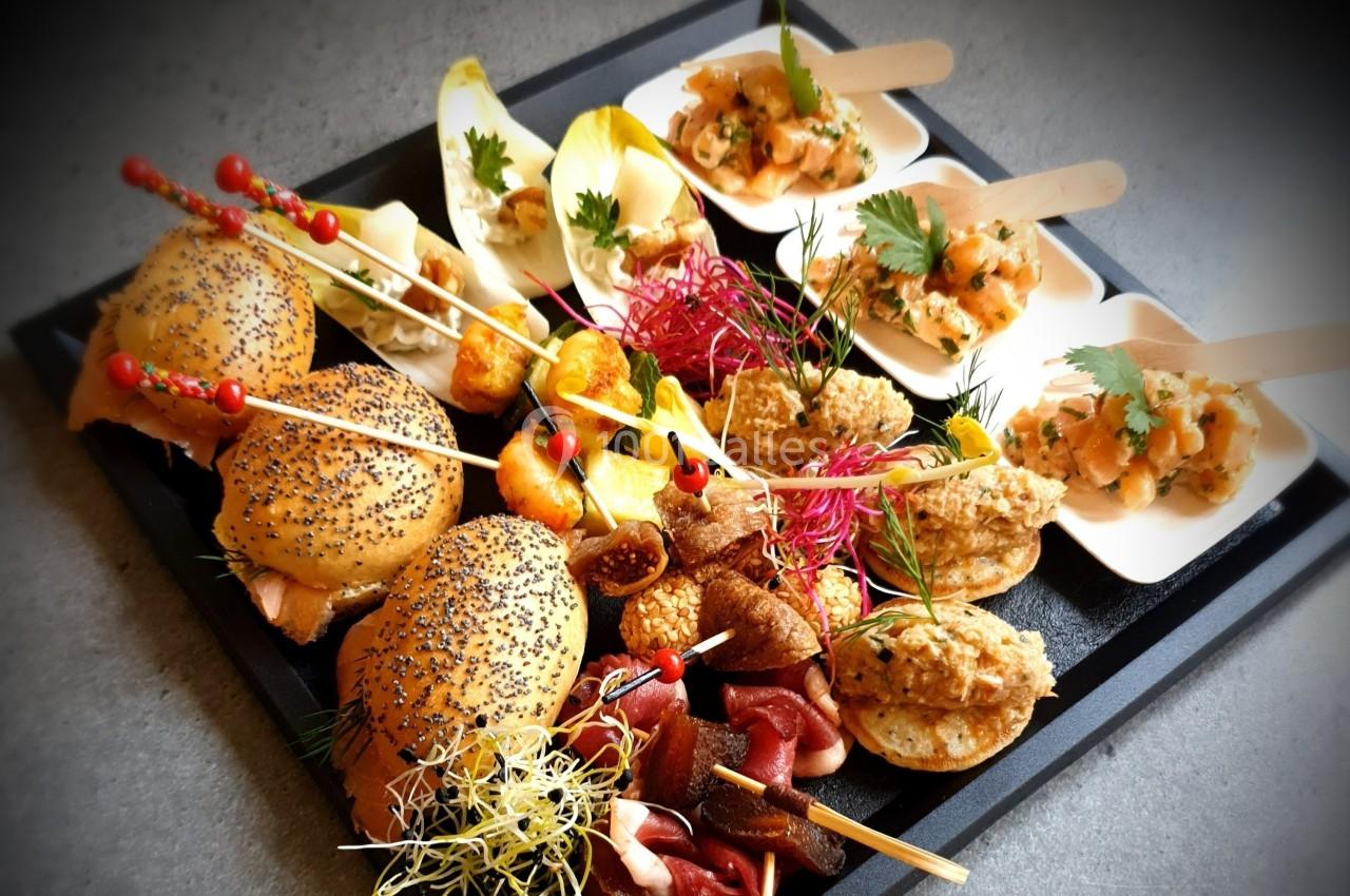 Plateau de bouchées variées comprenant mini-sandwichs, tartines, verrines et fruits, présenté sur un plateau noir.