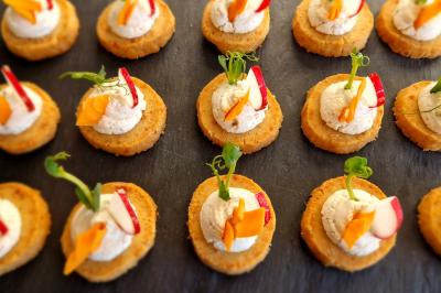 Assortiment de canapés sur une ardoise, garnis de crème et décorés de légumes colorés.