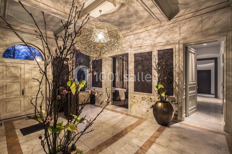 Entrée élégante avec sol en marbre, lustre design, branches décoratives et portes ouvertes sur un intérieur lumineux.