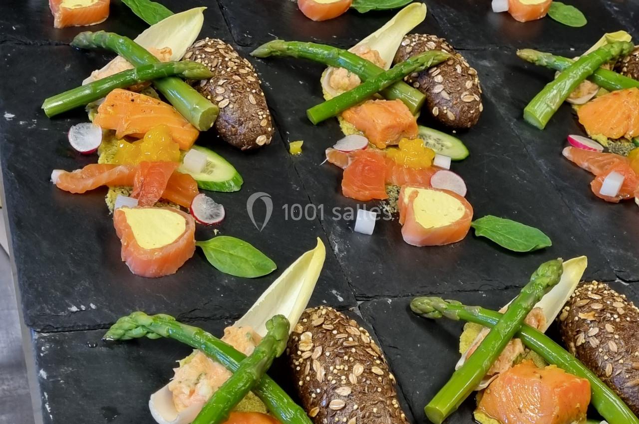 Assiettes dressées avec saumon fumé, asperges vertes, radis, pain aux graines et garnitures colorées sur ardoise noire.