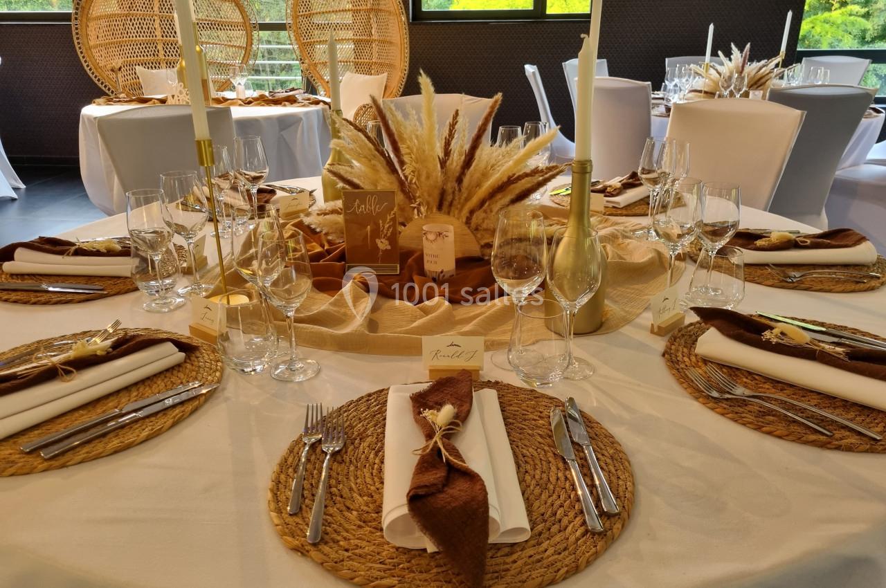 Table décorée pour un événement avec sets en rotin, serviettes brunes, bougies et centre de table en pampas.