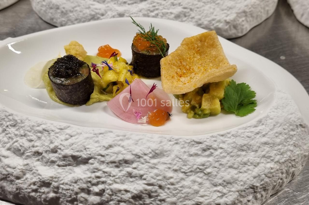 Assiette gastronomique avec des bouchées raffinées, incluant caviar, saumon, légumes et chips, présentée sur un plat texturé.