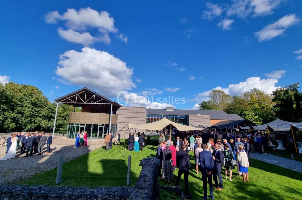 Groupe de personnes rassemblées en extérieur devant un bâtiment moderne, sous un ciel bleu avec quelques nuages.
