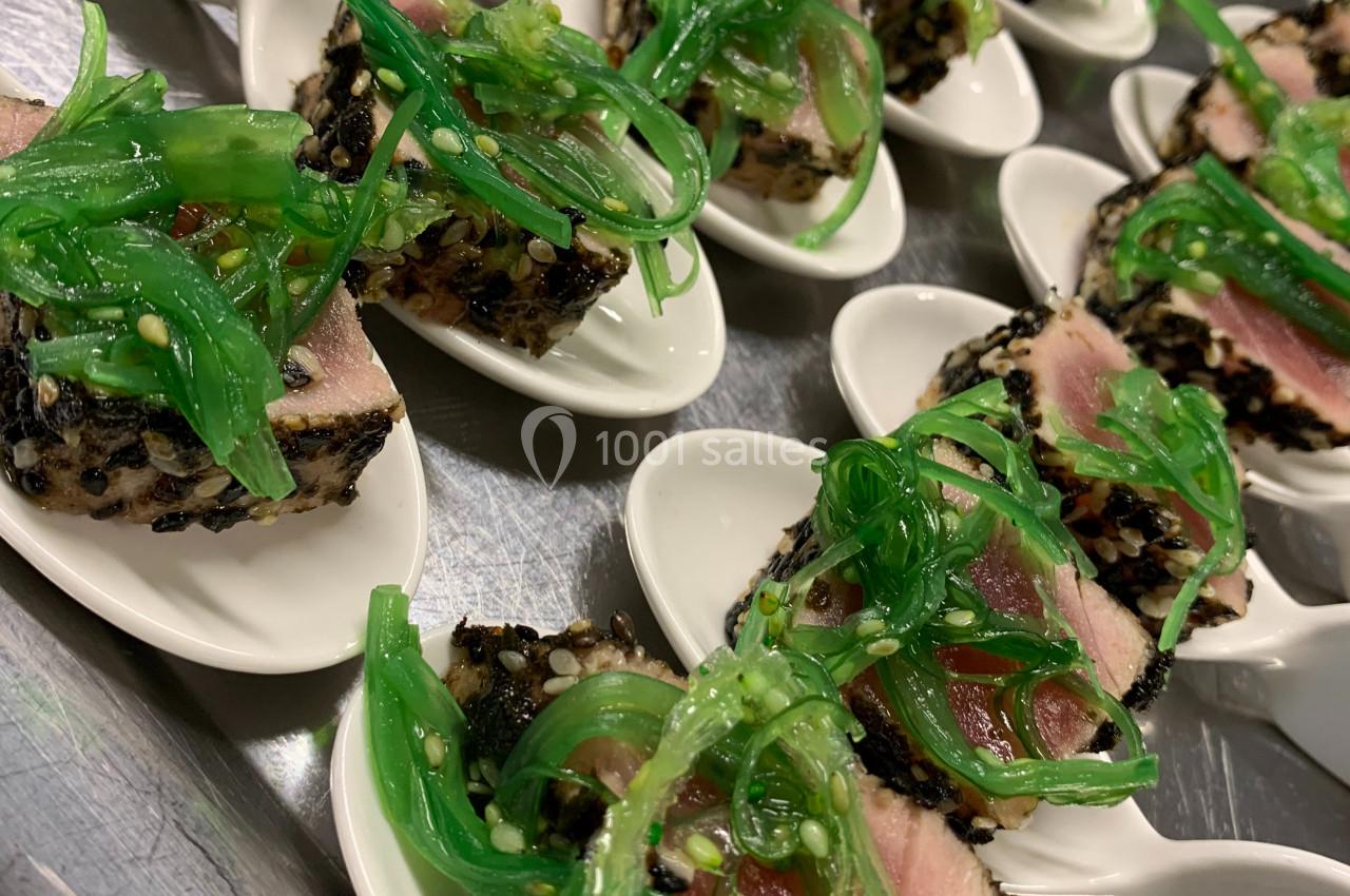 Tranches de thon mi-cuit en croûte de sésame noir, servies sur des cuillères avec une garniture d'algues vertes.