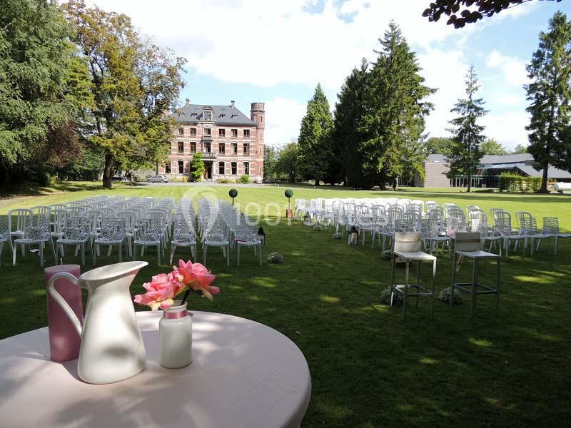 Chaises disposées en rangées sur une pelouse devant un château, avec une table décorée au premier plan.