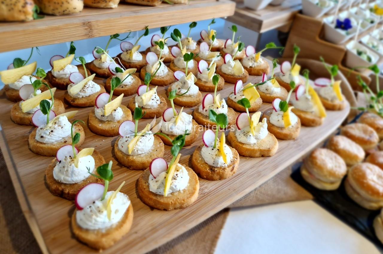 Plateau de canapés garnis de fromage frais, radis, herbes et chips, disposés sur une planche en bois.