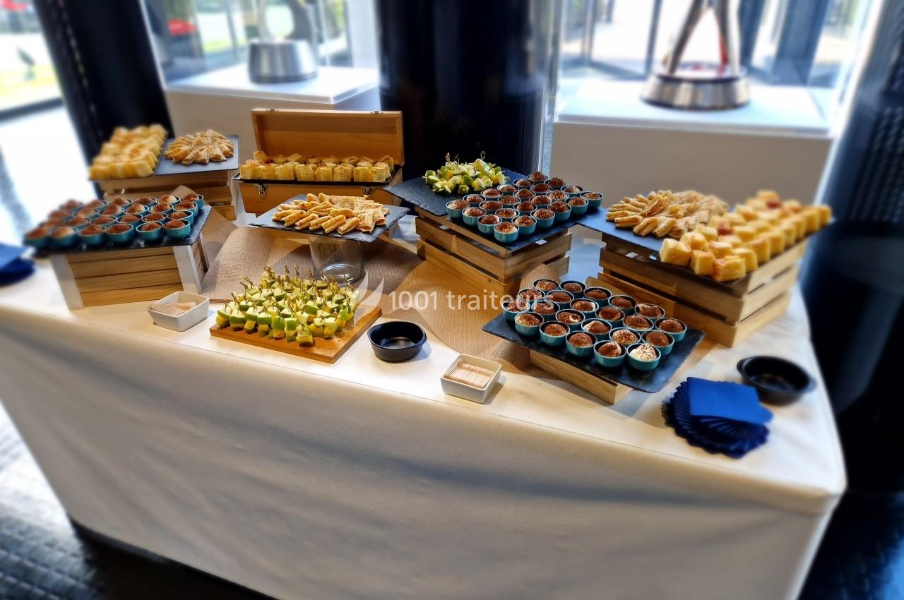 Buffet de verrines et amuse-bouches variés disposés sur des présentoirs en bois dans un cadre lumineux.