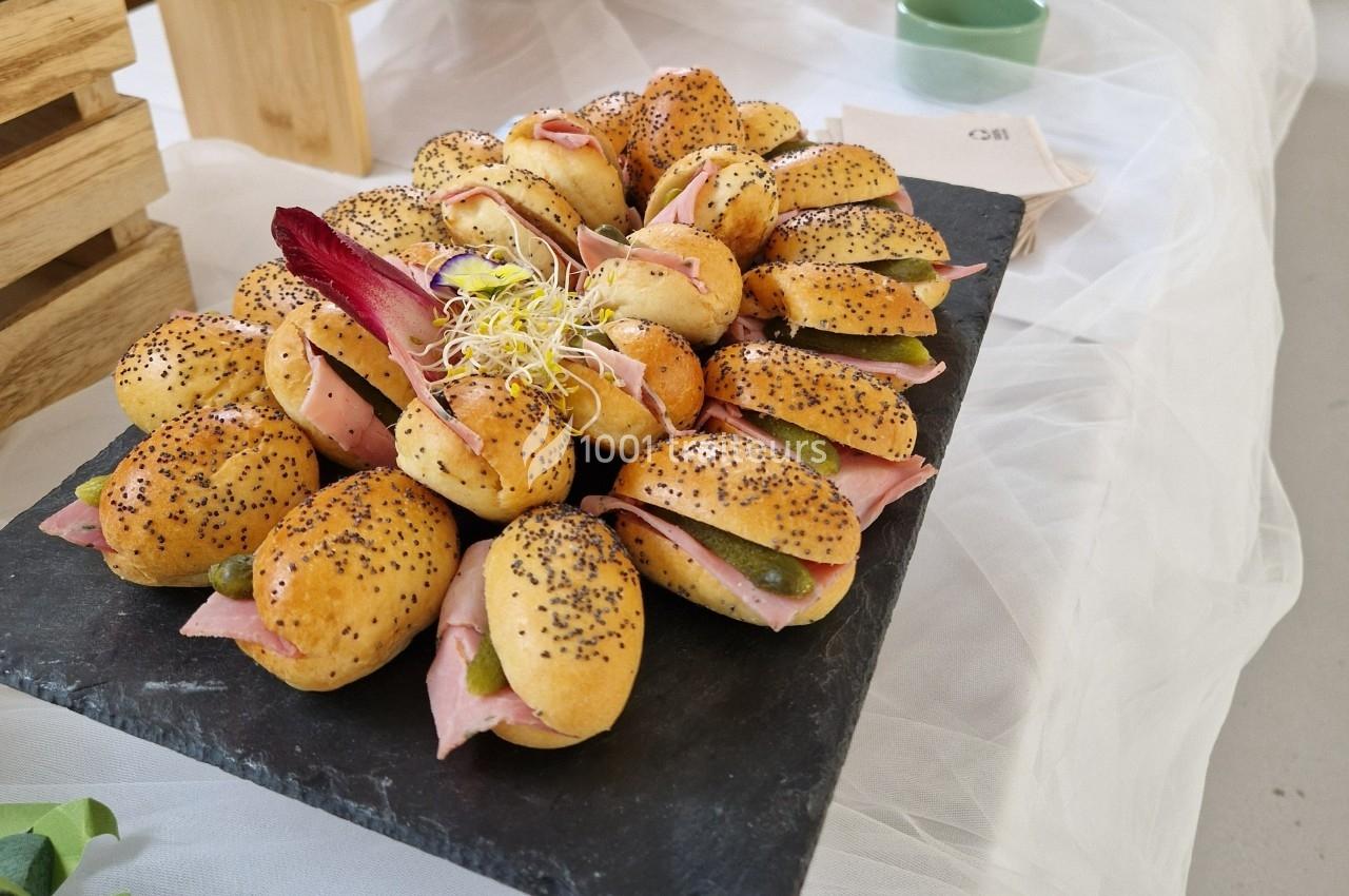 Plateau de mini-sandwichs garnis de jambon, cornichons et pousses, présentés sur une ardoise noire.