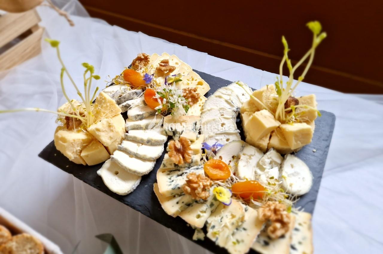 Plateau de fromages variés avec noix, abricots secs et décorations végétales sur une ardoise noire.