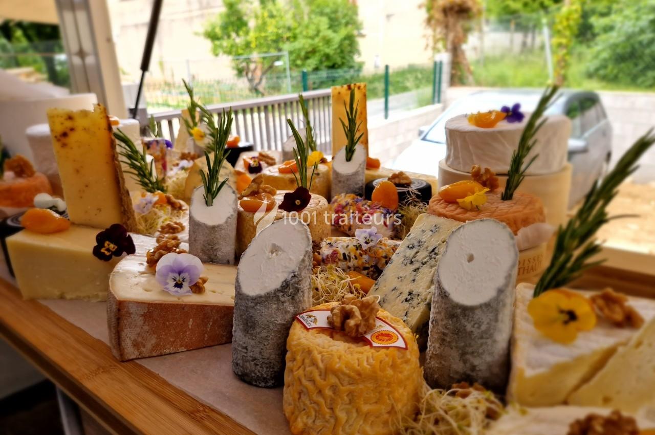 Plateau de fromages variés décorés de fleurs comestibles, noix et herbes, présenté sur une table en bois.