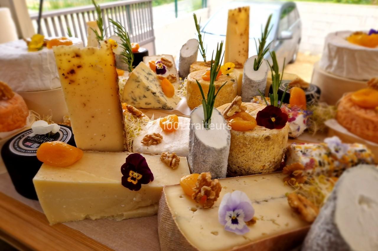 Plateau de fromages variés décorés de fleurs comestibles, noix et fruits secs, présenté sur une table en bois.