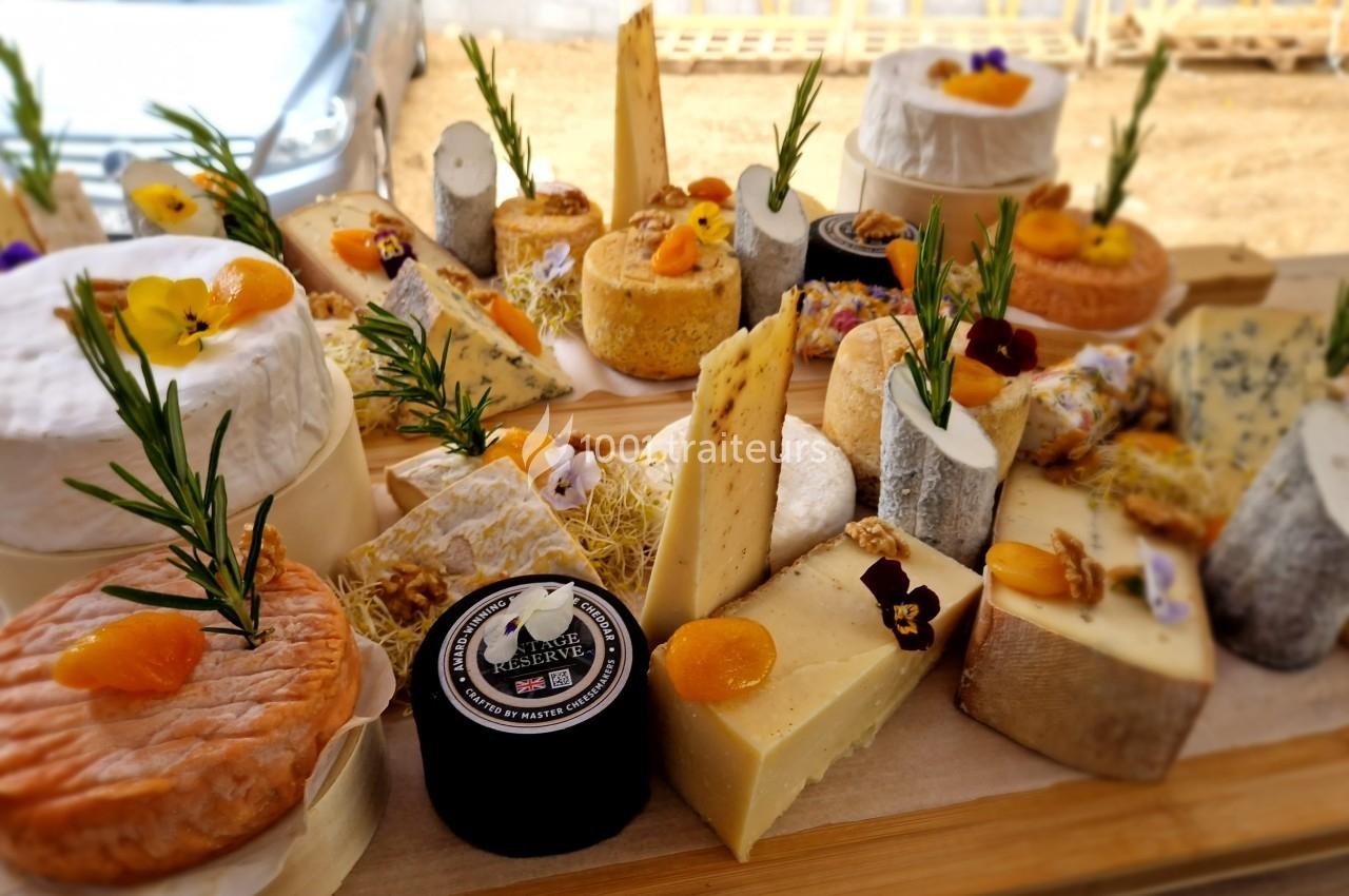 Plateau varié de fromages artisanaux décorés de fleurs comestibles et herbes fraîches, présenté sur une planche en bois.