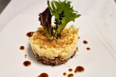 Plat dressé avec une base de viande effilochée, purée de pommes de terre, feuilles de salade et sauce en décoration.