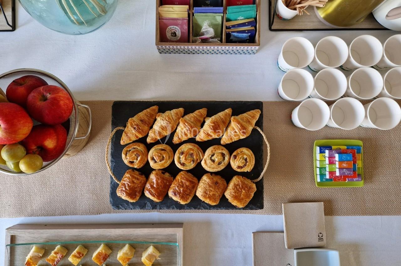 Plateau de viennoiseries variées sur une table dressée avec fruits, tasses et accessoires pour le petit-déjeuner.