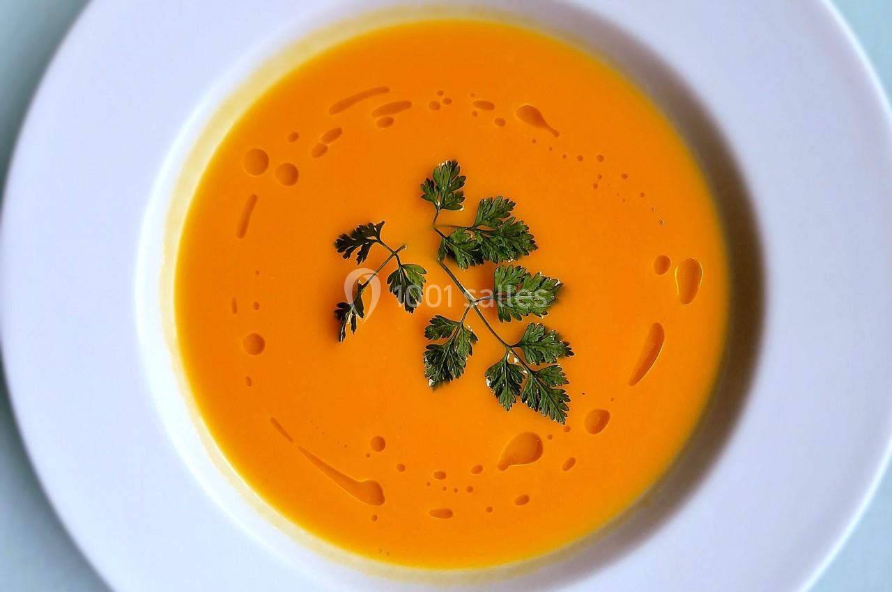 Bol de soupe orange crémeuse, décoré de feuilles de persil et de gouttes d'huile sur une assiette blanche.