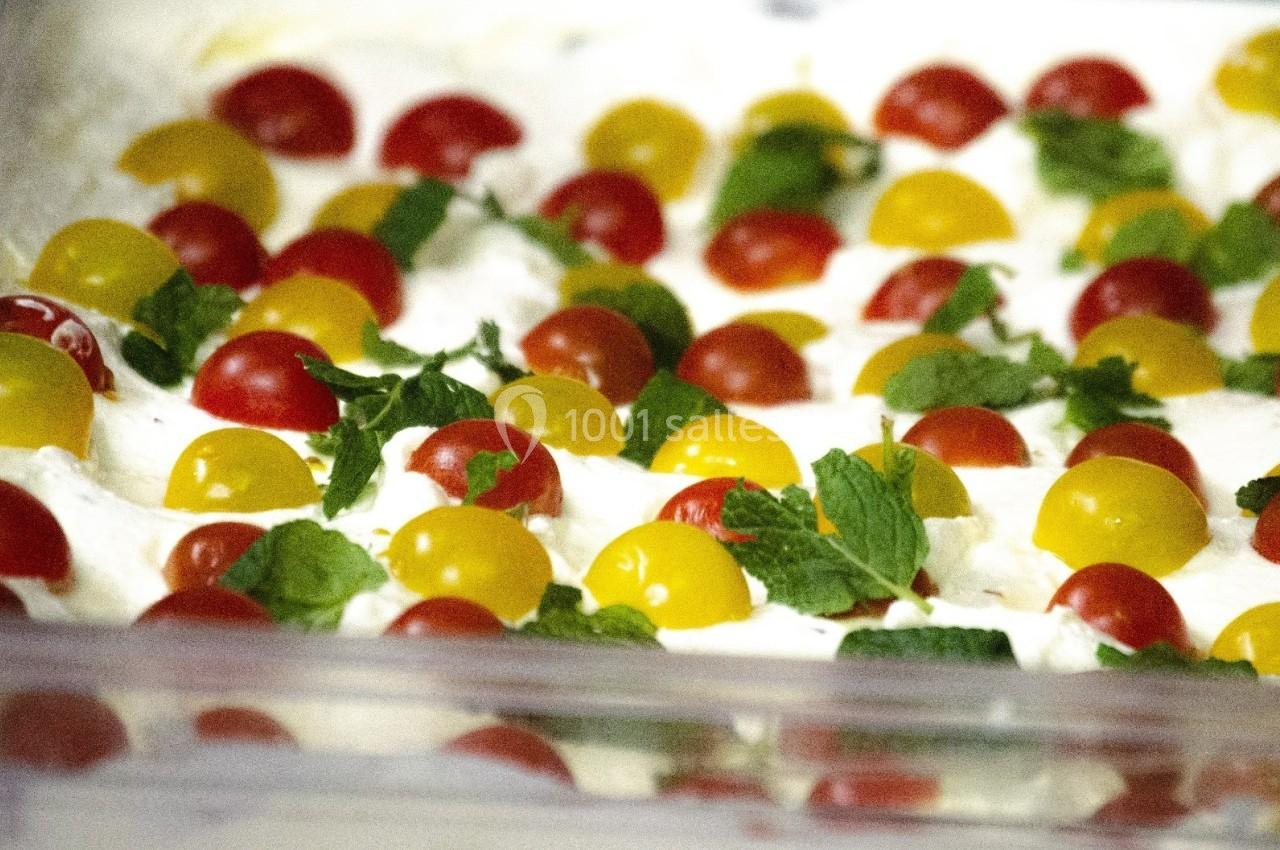 Tomates cerises rouges et jaunes disposées sur une base crémeuse, garnies de feuilles de menthe fraîche.
