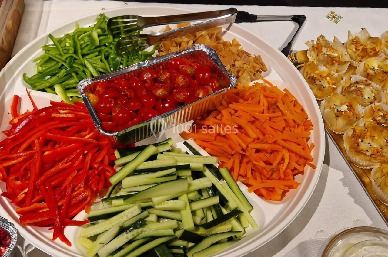 Plateau de crudités avec poivrons, carottes, concombres, tomates cerises et accompagnements variés sur une table.