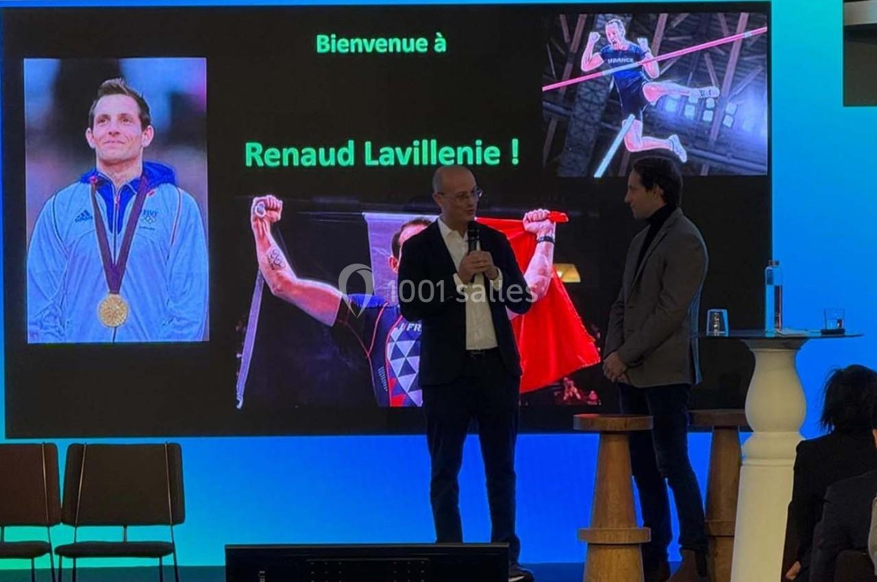 Deux hommes discutent sur scène devant un écran affichant des images de Renaud Lavillenie et un message de bienvenue.