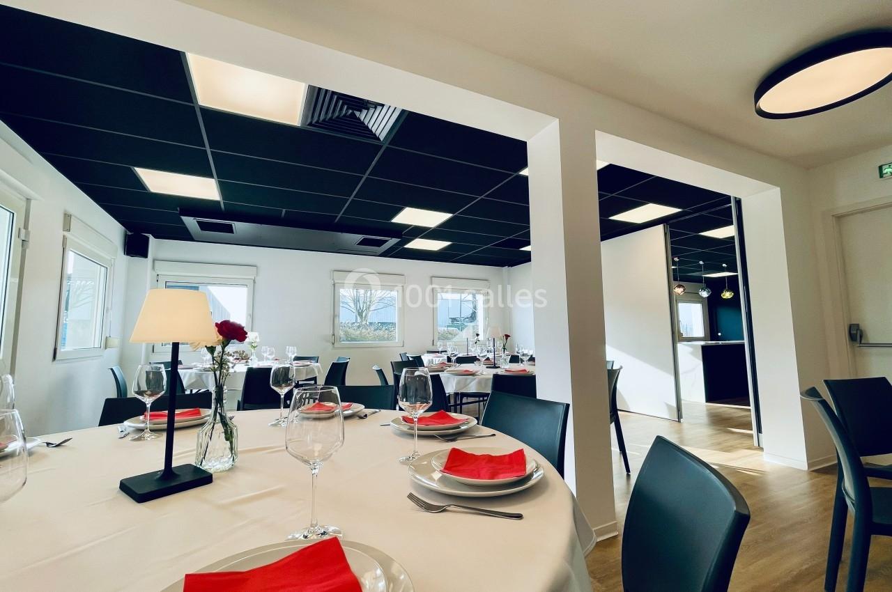 Salle de restaurant lumineuse avec tables dressées, nappes blanches, serviettes rouges et décoration élégante.