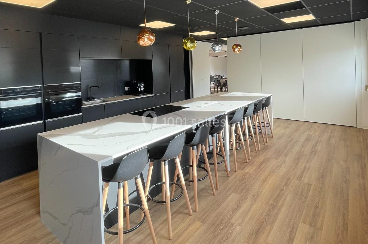 Cuisine moderne avec un long îlot central en marbre, tabourets noirs, éclairage suspendu et sol en bois clair.