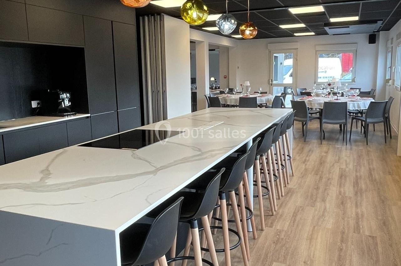 Cuisine moderne avec un îlot central en marbre, tabourets noirs, luminaires suspendus et salle à manger en arrière-plan.