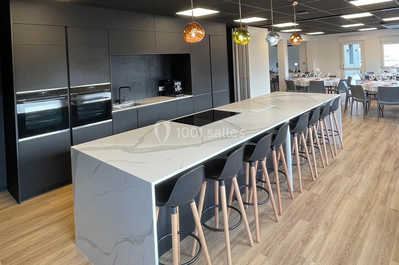 Cuisine moderne avec un grand îlot central en marbre, chaises hautes, éclairage suspendu et parquet clair.