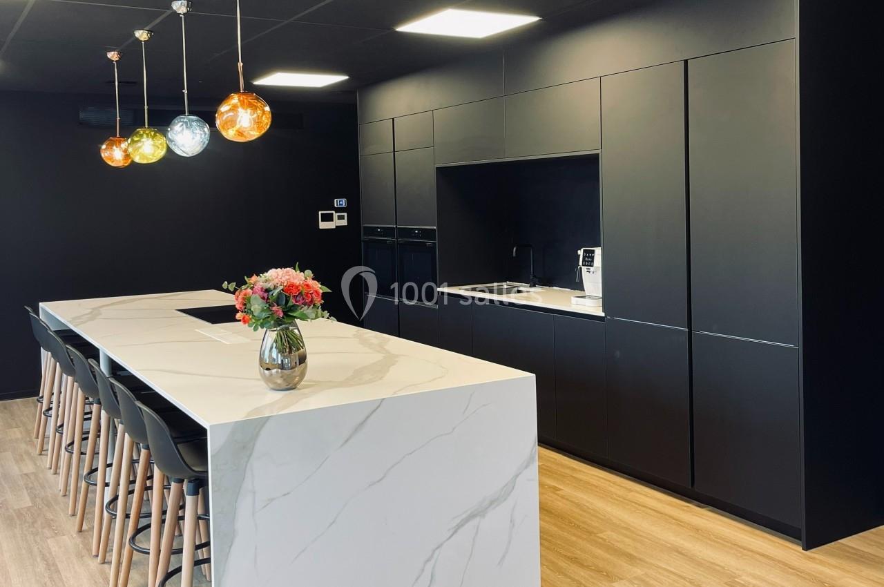 Cuisine moderne avec un îlot central en marbre, des armoires noires, des suspensions colorées et un bouquet de fleurs.