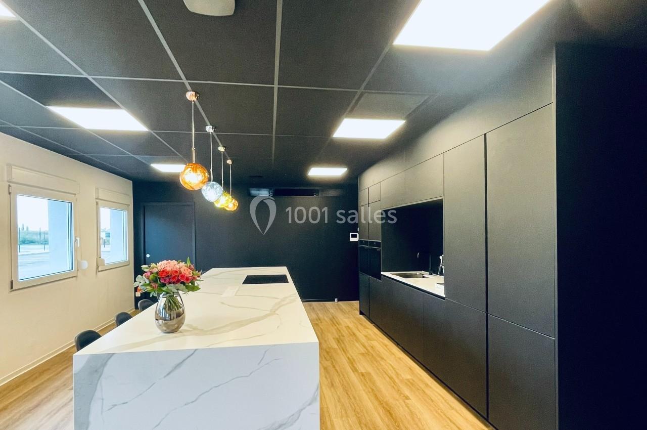 Cuisine moderne avec un îlot central en marbre blanc, éclairage suspendu coloré et mobilier noir mat.