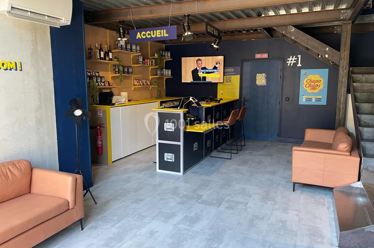 Espace d'accueil moderne avec comptoir, étagères de produits, canapés et écran diffusant une vidéo.