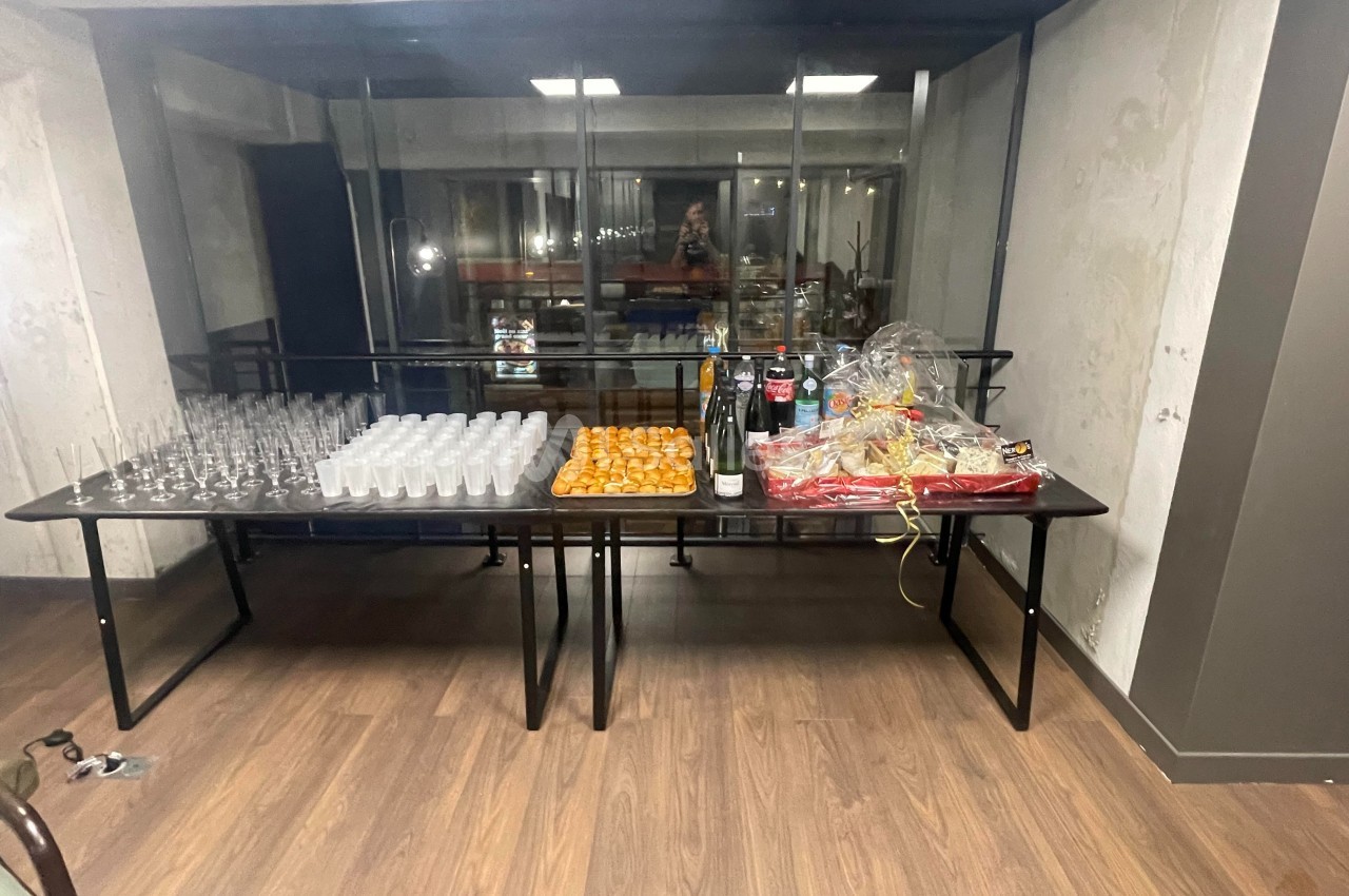 Table avec verres, boissons, plateaux de mignardises et paniers garnis dans une pièce au sol en bois.