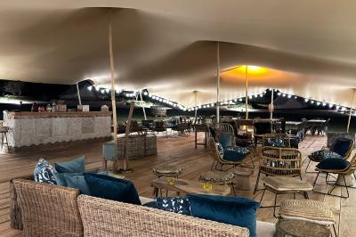 Fête nocturne en plein air avec un bar central, des invités debout et des lumières colorées sous une tente éclairée.